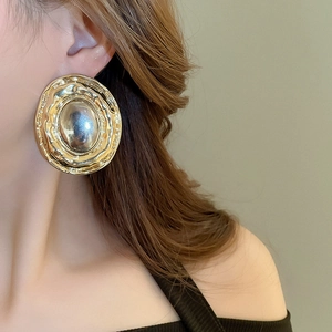 Detail of chunky gold disc earrings with textured wavy edges worn on a model's ear