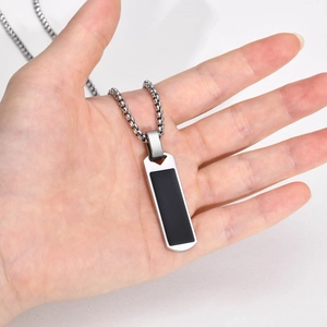 Close-up of a silver rectangular pendant with black inlay held by hand on a box chain