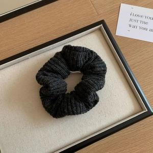 Détail d'un chouchou en maille noire avec texture tissée sur un plateau en lin