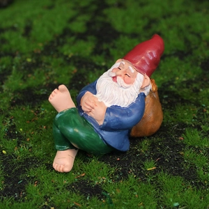Sleeping garden gnome resin statue with red hat and blue coat on green moss background