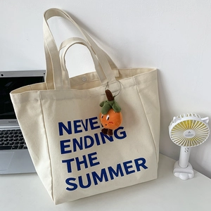 Detail of off-white canvas tote with blue lettering and orange persimmon plush charm