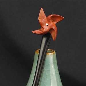 Close-up of a wood hair pin with a red windmill top in a green ceramic vase