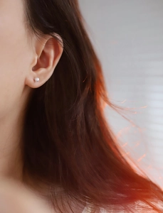 Detailed close-up of a mini white pearl stud earring worn on a model ear lobe