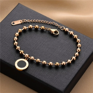 Close-up of rose gold beaded bracelet with black Roman numeral pendant on luxury velvet