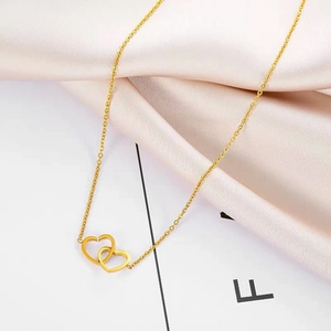 Close-up of golden double-heart pendant necklace displayed on soft pink silk fabric