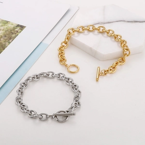 Detail of chunky gold and silver chain bracelets with toggle clasp on marble stand