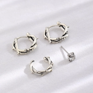 Gothic silver earring set featuring thorn hoops and a crystal stud on white fabric