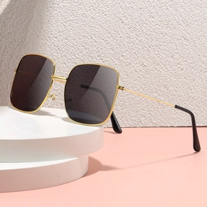 Retro oversized square sunglasses with gold metal frame and dark lenses on white pedestal