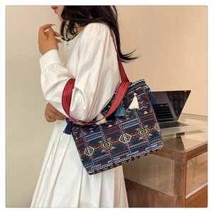 Ethnic tote bag with tassel and wide strap worn by model in a bright interior setting