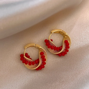 Close-up of twisted gold hoop earrings with woven red crystal beads on satin fabric