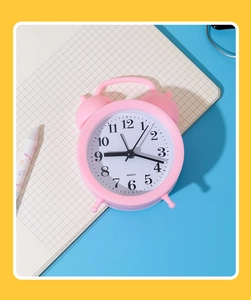Detailed view of a pink quartz twin-bell alarm clock on a blue desk with notebook