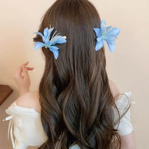 Close-up of a pair of light blue lily fabric hair clips worn on long wavy brown hair