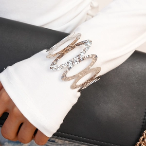 Detail of silver wavy hammered metal cuff bracelet worn over a white textured sleeve