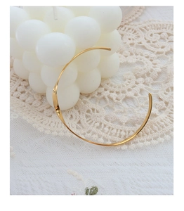Close-up of a minimalist twisted gold bangle wrapped around a white geometric candle