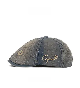 Detail view of washed blue denim flat cap with yellow embroidery on white background