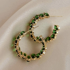 Vintage C-shaped gold hoop earrings with green rhinestones on beige silk fabric