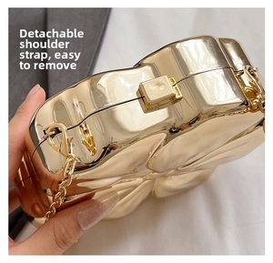 Detail of the golden floral-shaped metal evening bag showing the detachable chain strap