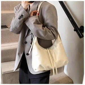 Cream-white soft leather tote bag with tassel detail shown on model in modern interior