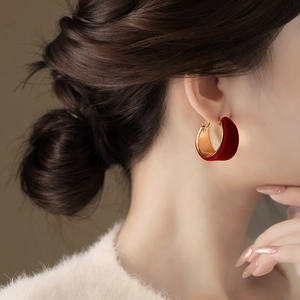 Close-up of model wearing gold-plated C-hoop earrings with elegant red velvet texture