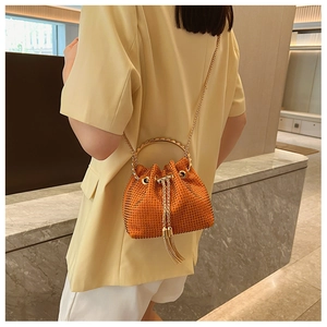Detail of orange rhinestone bucket bag with gold handle and chain on a stylish model