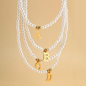 Detail of layered pearl necklaces with gold initial pendants A, B, C, and D