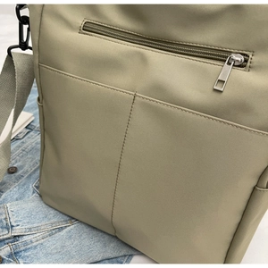 Detail of khaki nylon crossbody bag showing front zipper pocket and stitching textures