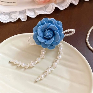Detail of blue denim fabric rose hair clip with white pearl tassels on lace background