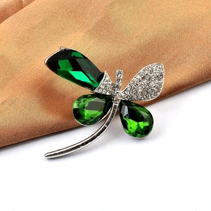 Macro shot of silver dragonfly brooch featuring green gems and pavé crystal wings