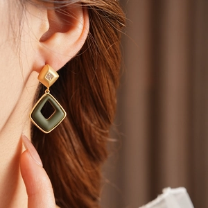Close-up of geometric diamond-shaped earrings in gold and dark green on model