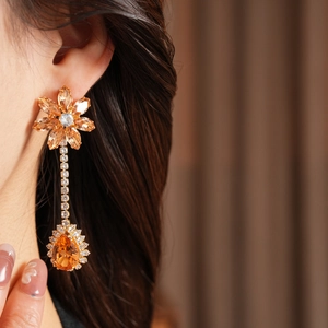 Detail of elegant gold drop earrings with orange gemstones and diamonds on model
