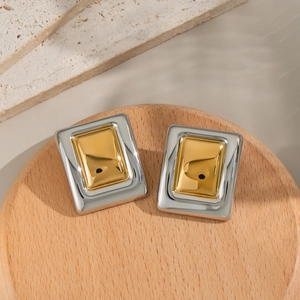 Detail of square gold and silver two-tone stainless steel stud earrings on wooden tray