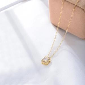 Close-up of golden necklace with emerald-cut zircon pendant on white silk background