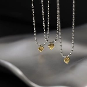 Macro shot of two-tone heart pendant necklaces featuring gold heart and silver bead chain