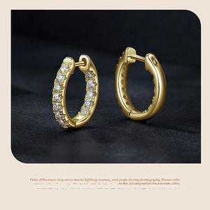 Close-up of gold huggie earrings with paved white stones on black background