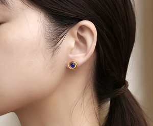Close-up of minimalist gold spiral earrings with a deep blue gemstone worn by a model