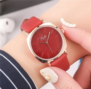 Close-up of a stylish gold square watch with a red leather strap on a woman's wrist
