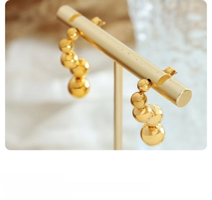 Detail view of gold sphere stud earrings featuring four graduated metallic beads on a stand