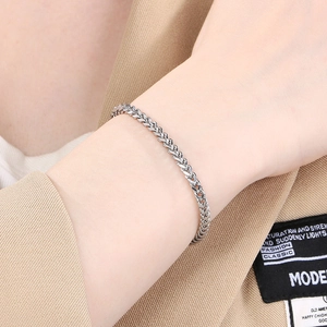 Gros plan d'un bracelet chaîne épi argenté porté au poignet avec un costume beige