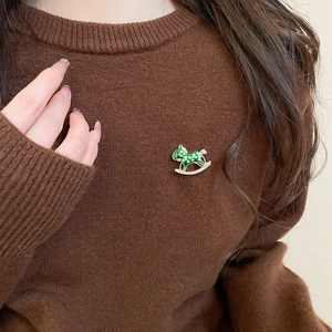 Detail of green enamel rocking horse brooch with diamonds on a brown sweater