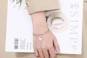 Close-up of a silver Hamsa Hand charm bracelet with hollow heart detail on a female wrist