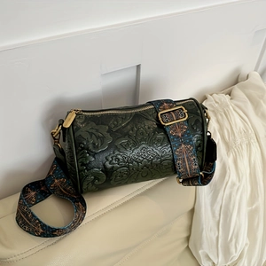 Close-up of dark green barrel bag with floral embossing and colorful woven shoulder strap