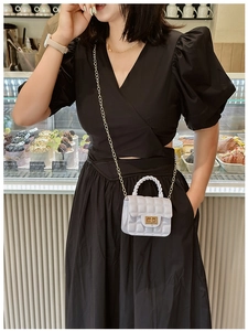Close-up of a white quilted jelly bag with gold hardware worn by a model in a cafe