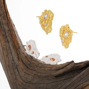 Irregular textured gold and silver stud earrings with zircon on a rustic wood base
