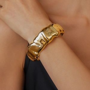 Macro shot of gold-plated bangle featuring unique irregular wavy surface and high-gloss finish