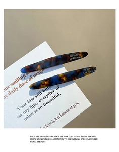 Detail of tortoise shell acetate hair clips with golden lettering on white card