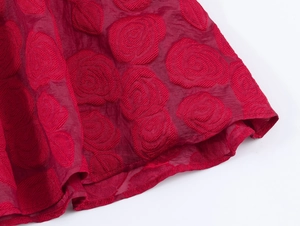 Gros plan du tissu jacquard rouge avec des motifs de roses 3D sur l'ourlet de la robe