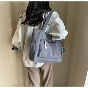 Detail of grey blue corduroy tote bag featuring front zipper pocket and decorative white tassel