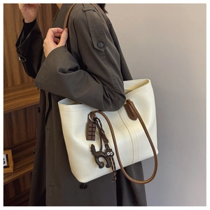 Detail of a cream leather tote bag with dark brown handles and a cute cat charm accessory