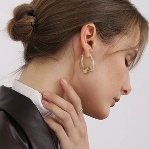 Irregular C-shaped gold bamboo earrings with radial shell texture on a model