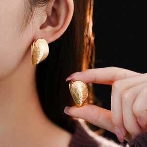 Close-up of golden shell-shaped earrings with textured metal finish worn by a model